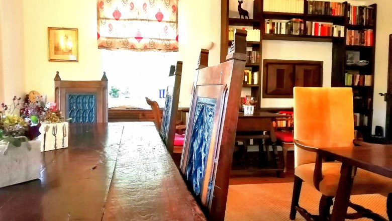 Frühstücksraum, © Landsitz Oberhof Ein gemütlicher Frühstücksraum mit Holztisch, blauen Stühlen, Bücherregal und dekorativem Fenster.