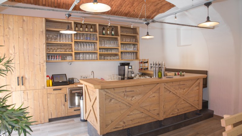 Stüberl, © Christian Piribauer Schank aus Holz mit Gläsern und Flaschen und Backsteindecke.