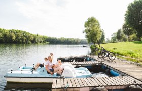 Entspannung im Freizeitzentrum Weitenegg, © NÖW_Stefan Fürtbauer Drei Personen auf einem Tretboot am See, Fahrräder am Steg, grüne Bäume im Hintergrund.