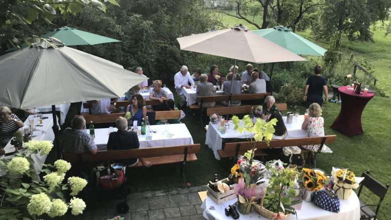 Festlich gedeckte Tische im Heurigengarten, © Monika Pölzer Menschen sitzen an festlich gedeckten Tischen im Freien unter Sonnenschirmen.
