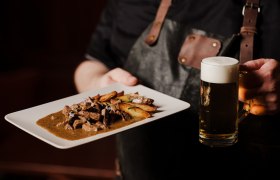 Gebratene Leber mit Bratkartoffeln, © Niederösterreich Werbung/Michael Reidinger Person hält Teller mit Fleischgericht und Bierkrug in der Hand.