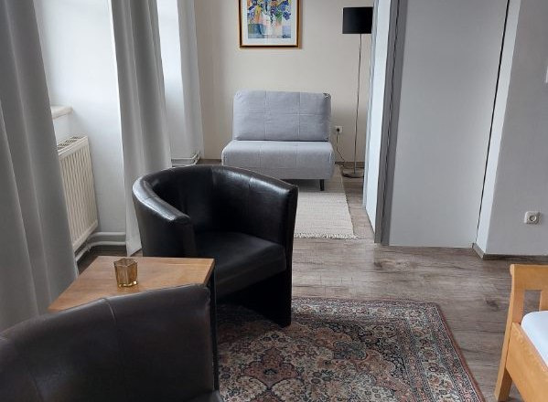 Gästezimmer Weixelbaum, © Familie Weixelbaum Modernes Gästezimmer mit zwei Ledersesseln, Teppich, grauem Sessel und Kunstwerk an der Wand.