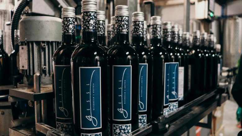Hervorragende Weine, © Bio Weingut Gessl Weinflaschen auf einem Förderband in einer Abfüllanlage.