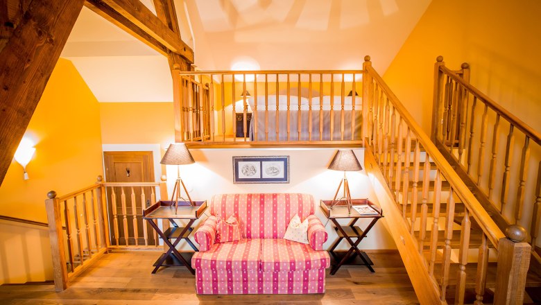 Romantiksuite, © Schlossschenke Gemütliche Suite mit Holzbalken, Treppe, Sofa und Lampen.