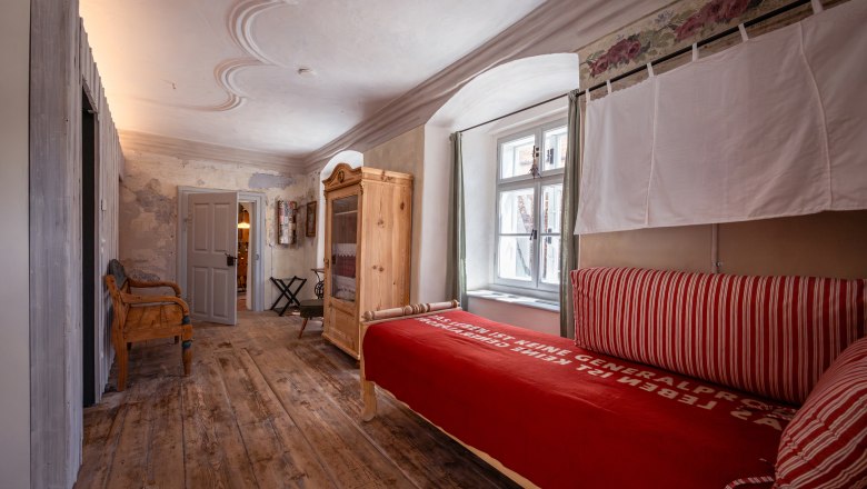 SONNENTOR Stadt-Lofts, © Niederösterreich Werbung / Maximilian Pawlikowsky Ein gemütliches Zimmer mit Holzboden, antikem Schrank und rotem Bett.