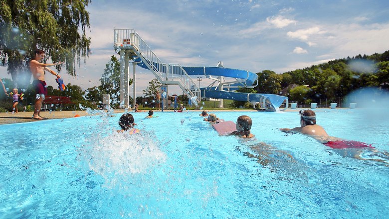Freibad Neuhofen an der Ybbs, © weinfranz Kinder schwimmen im Freibad Neuhofen an der Ybbs mit einer großen Wasserrutsche im Hintergrund.