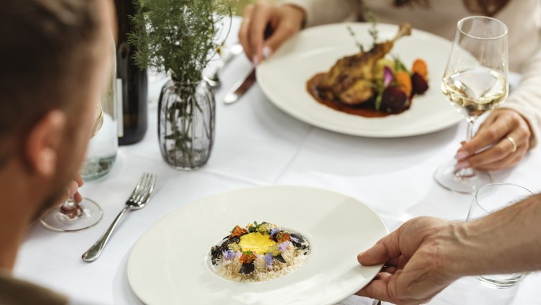 Genusswirtschaft Mailberg, © Weinviertel Tourismus / Michael Reidinger Ein elegantes Restaurantessen mit zwei Personen, die an einem Tisch sitzen. Ein Teller mit einem kunstvoll angerichteten Gericht wird serviert.