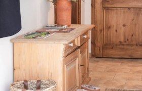 Vorraum, © Monika Pölzer Ein Vorraum mit Holzmöbeln, einem Korb, Stiefeln und einer Vase mit Blumen.