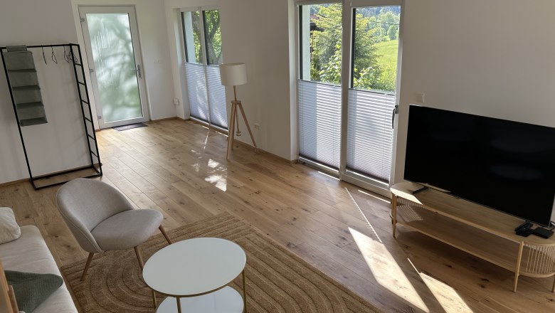 Tiny House, Feigenterrasse am Semmering, © Stupbacher Innenansicht eines modernen Wohnzimmers mit Holzboden, Sofa, Sessel, Couchtisch und Fernseher. Große Fenster lassen viel Licht herein.