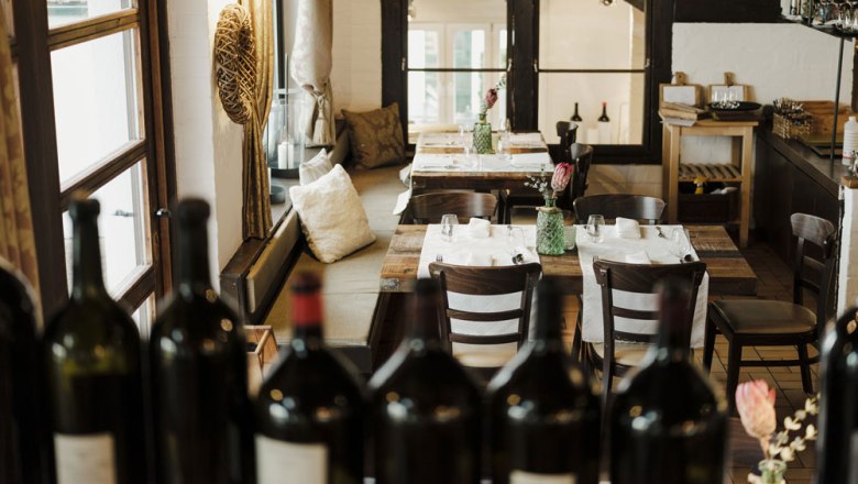 Große Weinexpertise, © Niederösterreich Werbung/Michael Reidinger Gemütliches Restaurant mit Holztischen und Weinflaschen im Vordergrund.