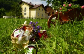 Bio Bauernhof Losbach, © zVg Ein gelbes Bauernhaus im Hintergrund, im Vordergrund ein Korb mit Gläsern und Flaschen auf einer Wiese.
