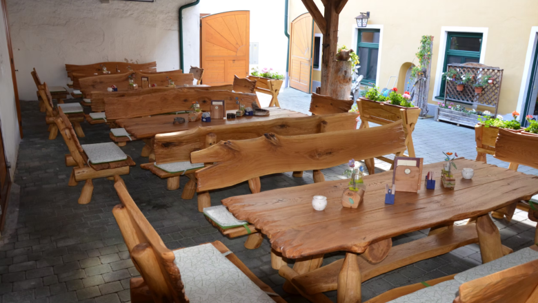 Gastgarten, © Gasthaus Georg Hacker Rustikale Holzbänke und Tische in einem Gasthaus-Innenhof mit Blumen und Dekorationen.