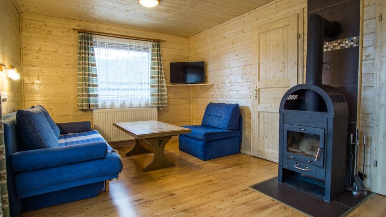 Ferienhaus "Romantik" Wohnzimmer, © Familie Morgenbesser Gemütliches Wohnzimmer mit Holzwänden, blauen Sofas, Holztisch und Kaminofen.