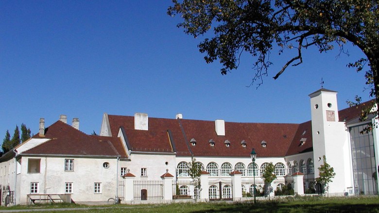 Das Freiherr von Joksch - direkt im Schloss Katzelsdorf, © Gemeinde Katzelsdorf Schloss Katzelsdorf mit rotem Dach und weißen Wänden, umgeben von Bäumen und Rasen.