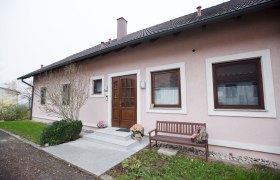 Ferienwohnung Muck, © schwarz-könig.at Eingang einer rosa gestrichenen Ferienwohnung mit Holztür, zwei Fenstern und einer Holzbank daneben.