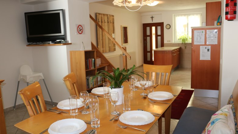 Essbereich Kueche Eingang Gaeste 6, © Gruber Claudia Essbereich mit gedecktem Tisch, Fernseher, Bücherregal und Küche im Hintergrund.