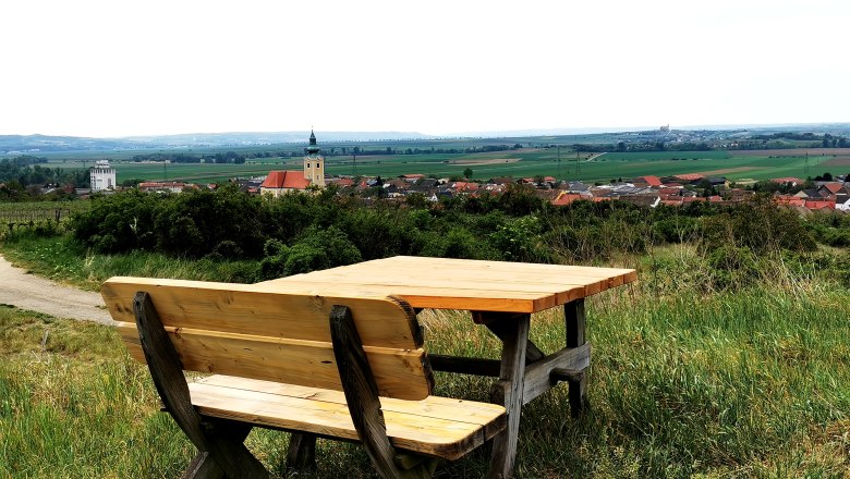 Rastplatz bei der Weinviertelwarte, © Weinstraße Weinviertel Holzbank mit Tisch auf einem Hügel mit Blick auf Röschitz und umliegende Landschaft.