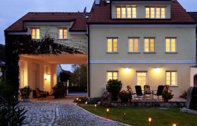 Pension Seyring, © Fam. Dungl Beleuchtetes Gebäude mit gepflastertem Weg und Gartenmöbeln im Vordergrund.