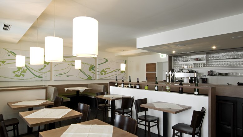 Restaurant Zur Schonenburg, © Gasthof Hotel "Zur Schonenburg" Innenansicht eines modernen Restaurants mit Holztischen, Stühlen und einer Bar mit Flaschen und Gläsern.