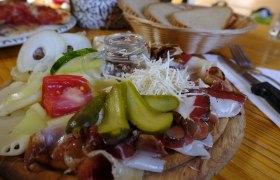 Symbolbild, © Pixapay Ein rustikales Brett mit Käse, Schinken, Gurken, Tomaten und Zwiebeln, serviert mit Brot im Hintergrund.