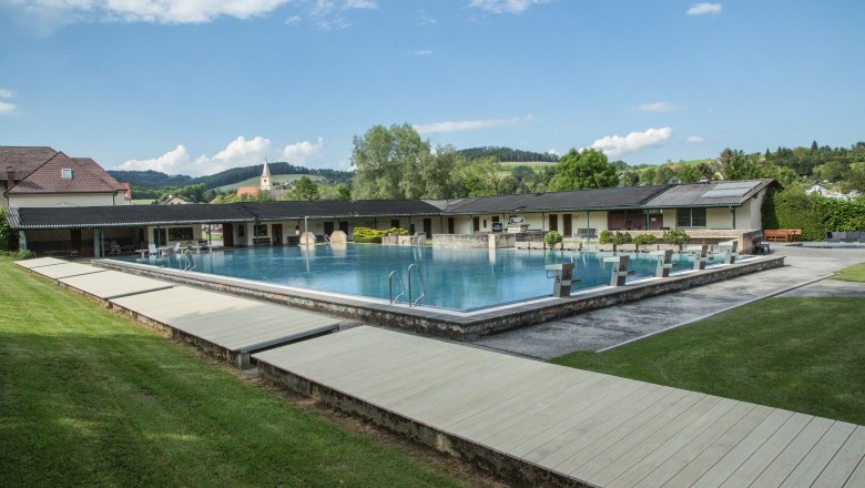 Freibad Krumbach, © SchwimmbadKrumbach©Marktgemeinde Krumbach, Foto: Franz Riegler Freibad Krumbach mit Schwimmbecken und Sprungblöcken, umgeben von grüner Landschaft und Gebäuden.