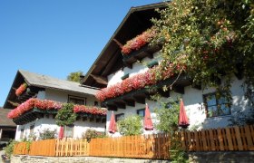 Leitnerhof, © zVg Rosenbaum Traditionelles Bauernhaus mit Blumen an den Balkonen und einem Holzzaun im Vordergrund.