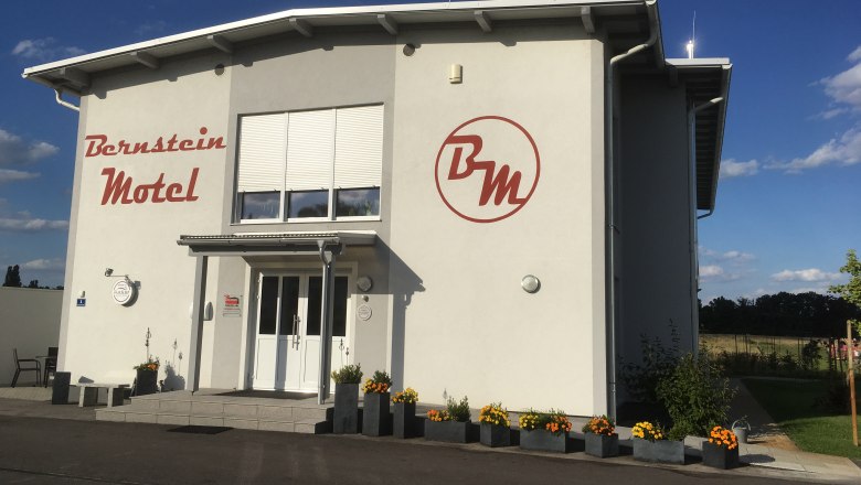 Bernstein Motel, © Bernstein Motel Außenansicht des Bernstein Motels mit Blumen und blauem Himmel.