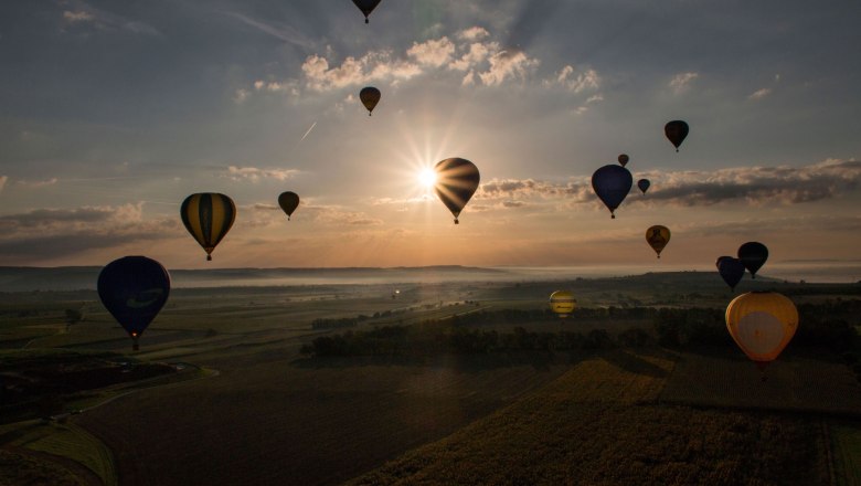 Ballontage Krems-Langenlois 2016, © Jürgen Übl Heißluftballons schweben bei Sonnenaufgang über eine Landschaft.