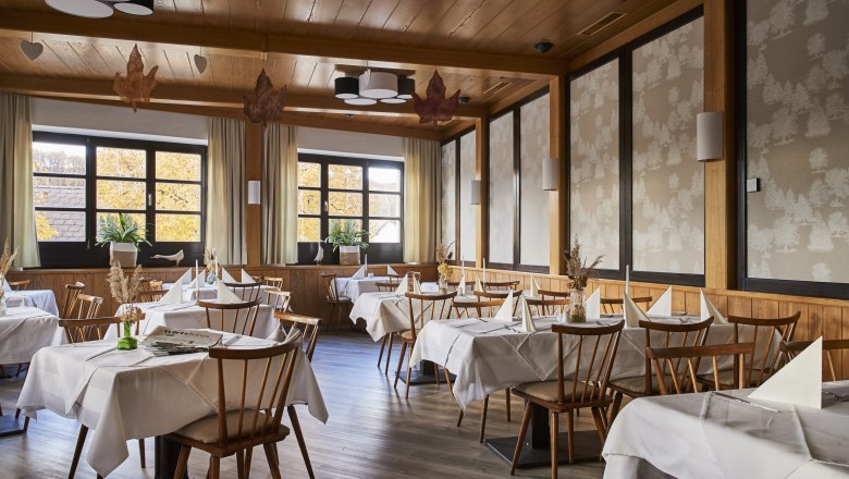 Helles, zeitloses Ambiente, © Niederösterreich Werbung/Andreas Hofer Ein elegantes Restaurant mit Holzmöbeln, weißen Tischdecken und großen Fenstern, die herbstliche Bäume zeigen.