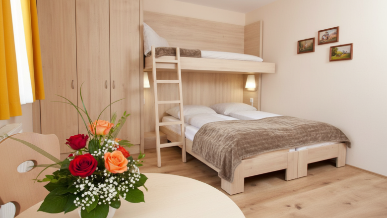Dreibettzimmer, © Austria-Best-Hotels Ein gemütliches Hotelzimmer mit einem Doppelbett und einem Hochbett, einem Holztisch mit Blumenstrauß und einem Kleiderschrank.