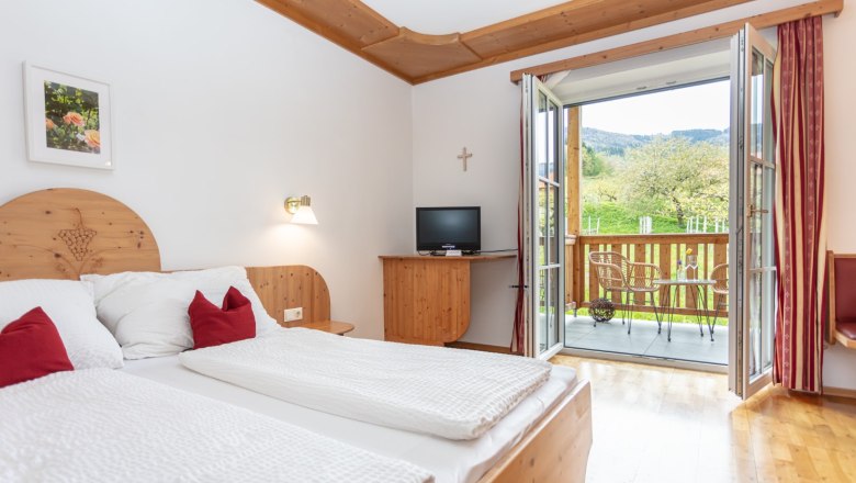 Doppelzimmer mit Balkon, © Weingut Rixinger Ein gemütliches Doppelzimmer mit Holzmöbeln, einem Balkon mit Blick ins Grüne und einem kleinen Fernseher.