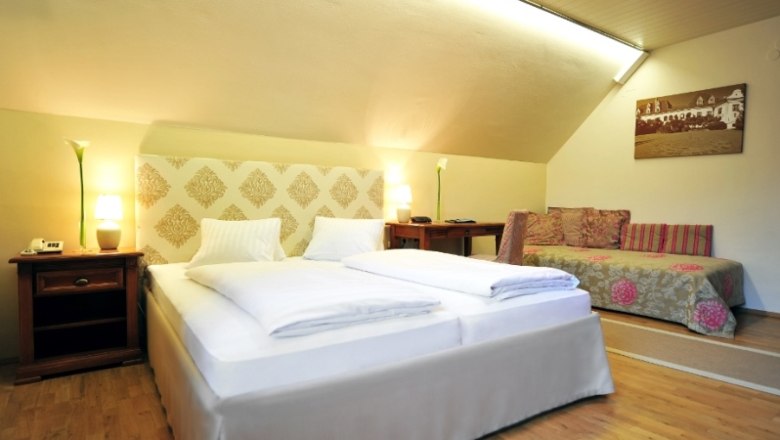 Renaissancehotel Raffelsberger Hof, © Renaissancehotel “ Raffelsberger Hof “ Hotelzimmer mit Doppelbett, Sofa und Holzmöbeln.