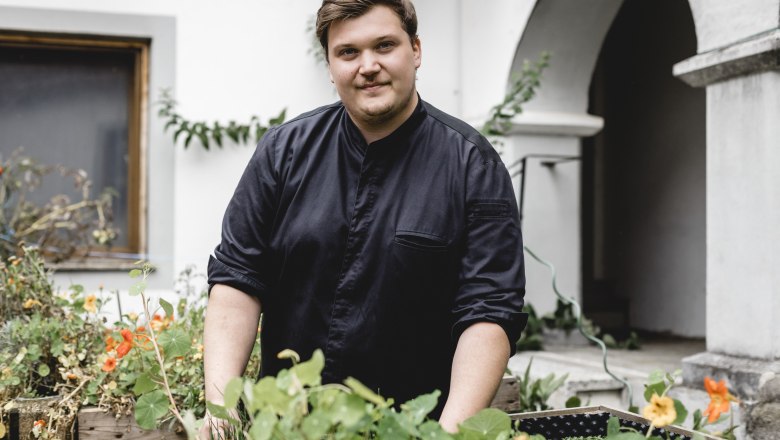 Reinhard Bürgmayr Junior, © Niederösterreich Werbung/David Schreiber Ein Mann in schwarzer Kleidung steht in einem Garten mit Blumen und Pflanzen.