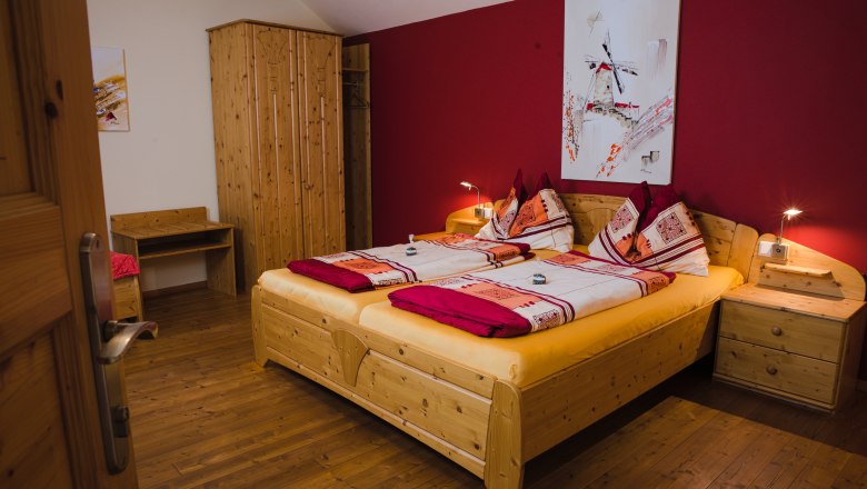 Gästezimmer, © Christoph Wurst Gemütliches Gästezimmer mit Doppelbett, Holzmöbeln und roter Wand.