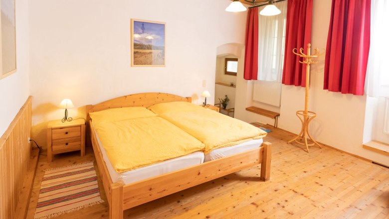 Schlafzimmer, © Fam. Zangl Gemütliches Schlafzimmer mit Holzmöbeln, gelber Bettwäsche und roten Vorhängen.