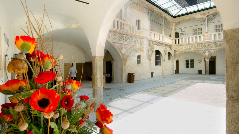 Arkadenhof, © Marktgemeinde Pöggstall Ein historischer Arkadenhof mit verzierten Wänden und einem Blumenarrangement im Vordergrund.