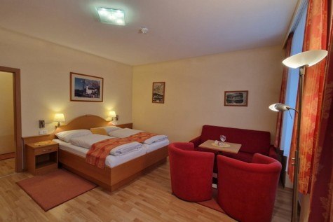 Kirchenwirt - Hotel - DZ Schneeberg, © Karin Stranz Hotelzimmer mit Doppelbett, rotem Sofa und Sesseln, Holzboden und Wandbildern.