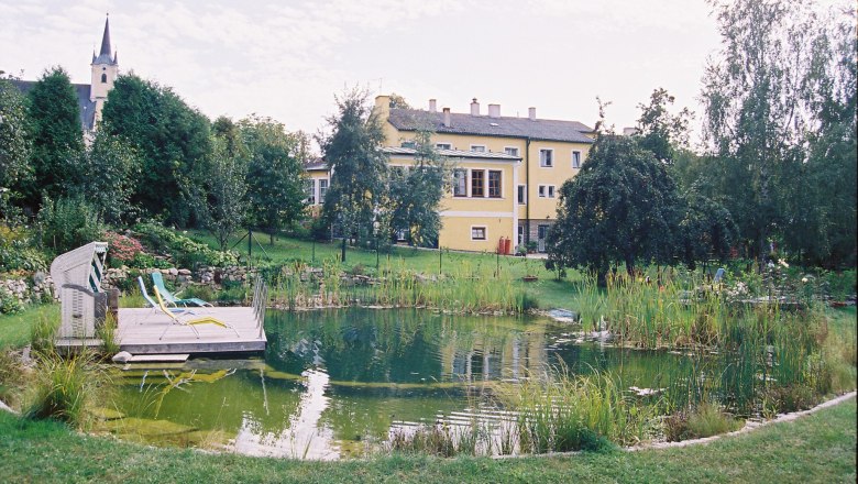 Schwimmbiotop im großen Naturgarten, © Ludwig Schneider Ein Schwimmbiotop in einem großen Garten mit einem gelben Gebäude im Hintergrund.