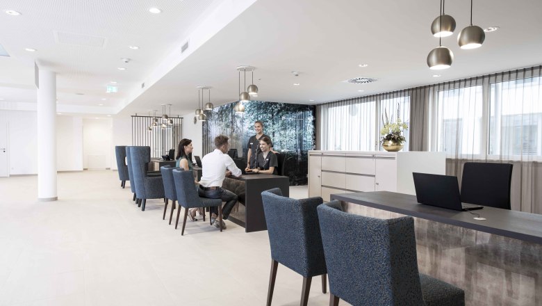 Rezeption, © NMC Moderne Rezeption mit Menschen, die an einem Tisch sitzen und sprechen.