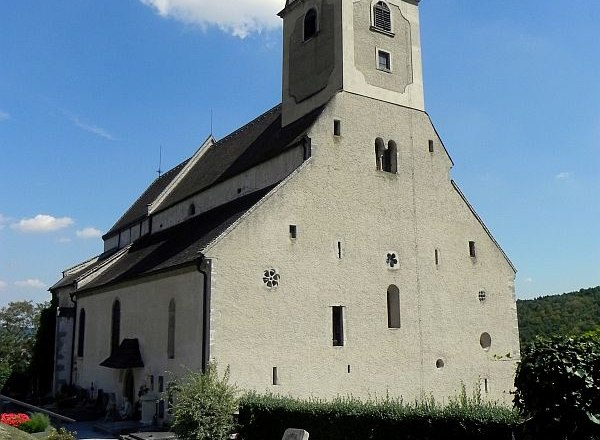 Gertrudskirche, © Gemeinde Gars Eine historische Kirche mit einem Turm und umliegendem Friedhof bei klarem Himmel.