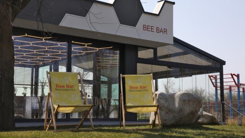 Bee Bar mit Relax-Stühlen, © Einhard Giehrl Zwei gelbe Liegestühle vor der Bee Bar mit Glasfassade und geometrischem Dach.