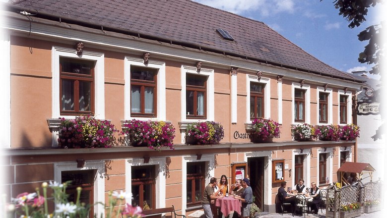 Marschall Stuben, © Marschall Stuben Ein traditionelles Gasthaus mit blumengeschmückter Fassade und Gästen, die draußen an Tischen sitzen.