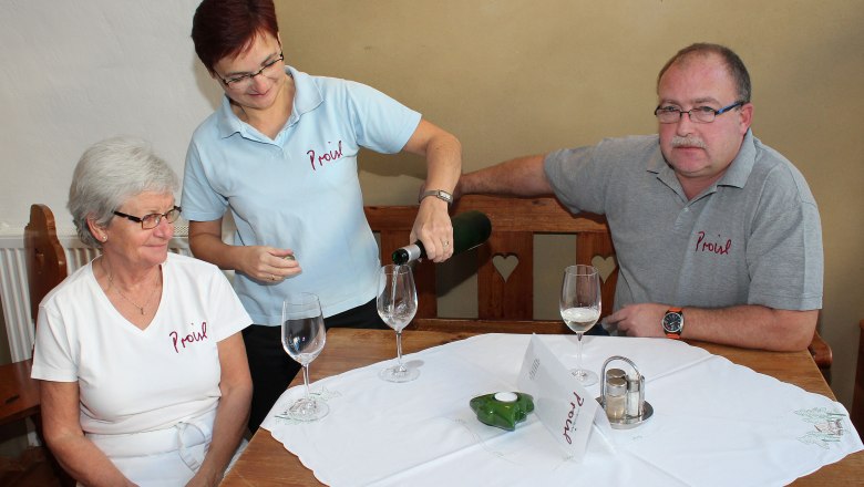 Familie, © Weinbau Proisl Drei Personen sitzen an einem Tisch, eine Frau schenkt Wein ein.