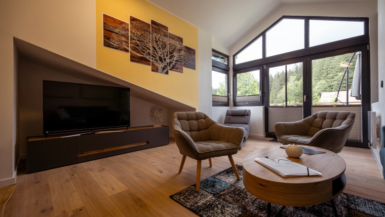 Ötscher Lodge, © Niederösterreich Werbung / Maximilian Pawlikowsky Modernes Wohnzimmer mit großen Fenstern, zwei Sesseln, einem Fernseher und einem runden Couchtisch.