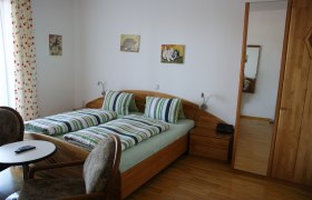 Privatzimmer Würger, © Privatzimmer Würger Ein gemütliches Schlafzimmer mit einem Doppelbett, gestreifter Bettwäsche, zwei Stühlen und einem kleinen Tisch. An der Wand hängen Bilder.