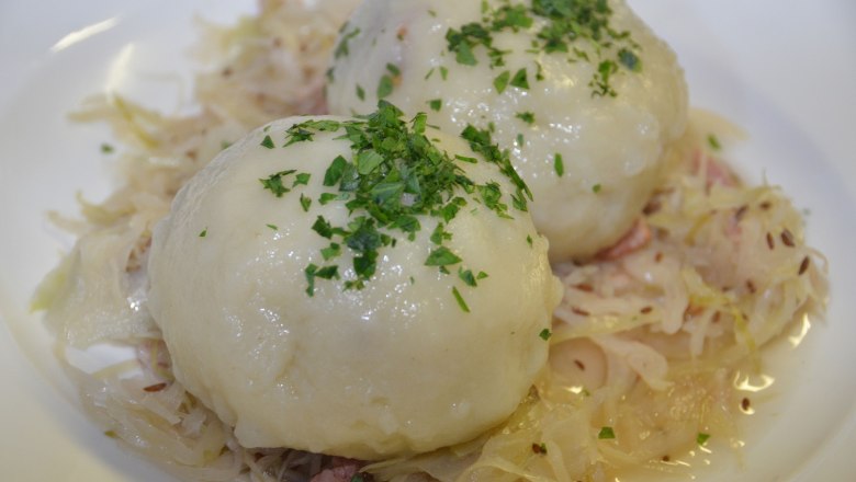 Grammelknödel, © Weinstube Aichinger Zwei Grammelknödel auf Sauerkraut, garniert mit Petersilie.