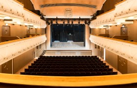 Prunkvoller Zuschauerraum: Wo Kultur auf bernsteinfarbenen Sitzreihen glänzt, © Alex Schwarz Photography Innenansicht des prachtvollen Stadttheaters Wiener Neustadt mit goldgelben Samtsesseln, Logen und funkelndem Kronleuchter