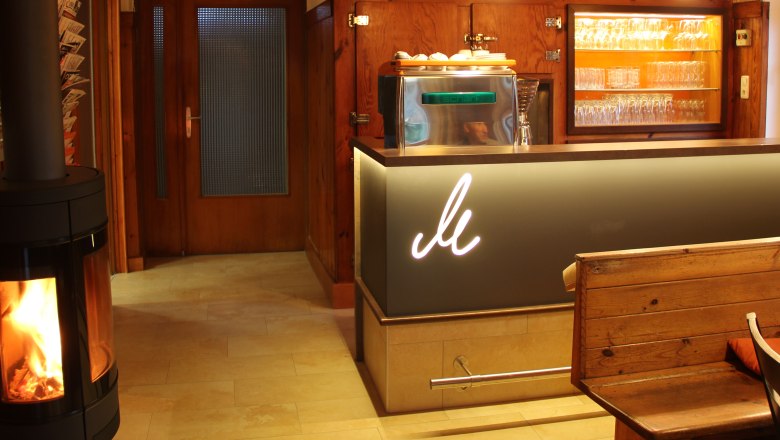 Schank, © Mühlendorfer Michael Gemütliche Bar mit Holzdekor, Kamin und Gläsern.