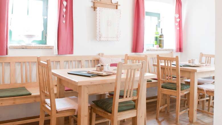 Heuriger zum Baumbart, © Bernd Baumgartner Gemütlicher Gastraum mit Holzmöbeln, roten Vorhängen und Dekoration.