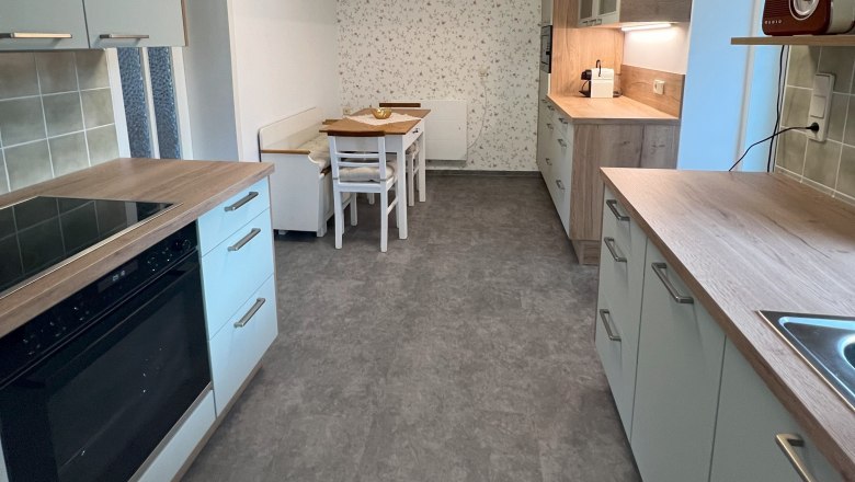 Küche, © Waltraud Forstner Moderne Küche mit grauen Schränken, Holzakzenten und einem Esstisch. An der Decke eine geometrische Lampe.